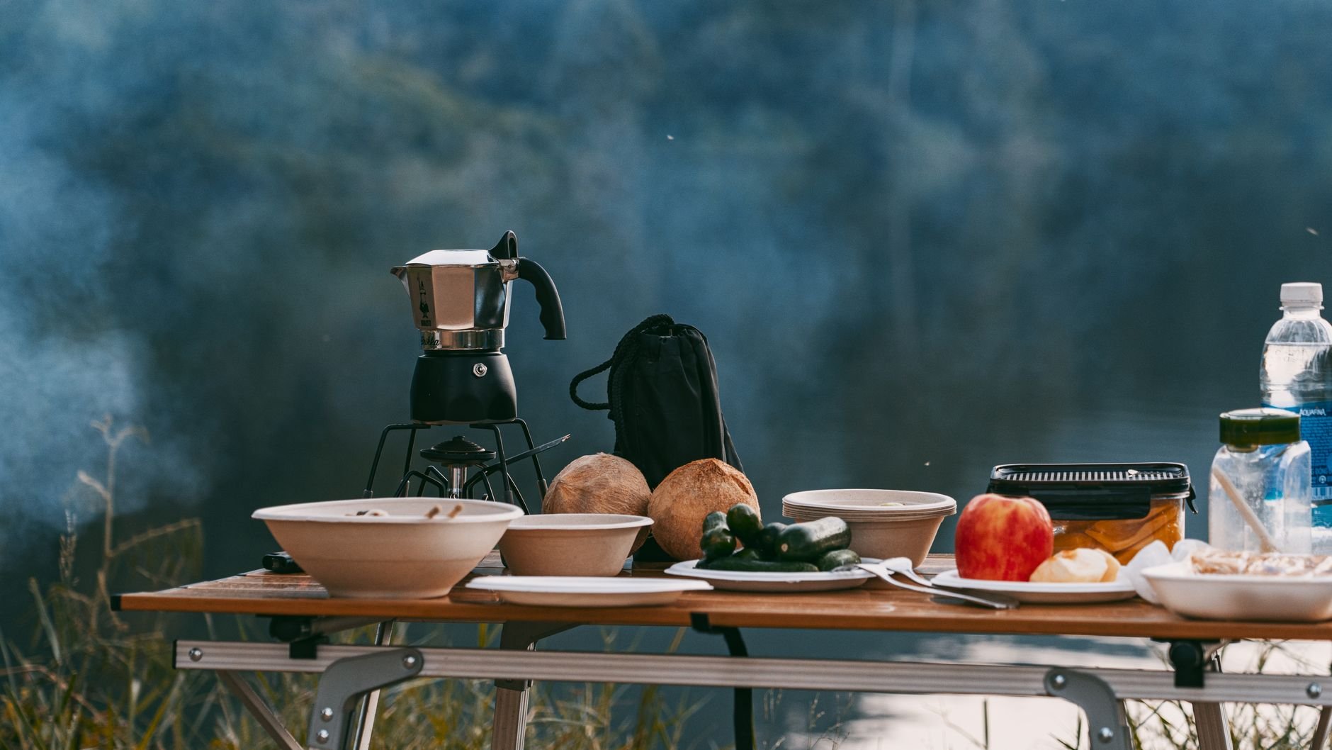 Outdoor breakfast by a lake with a coffee maker on a camping table